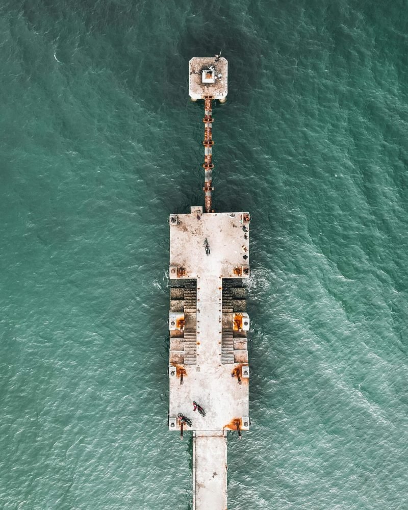 Drone shot of a weathered pier extending into the turquoise sea, highlighting marine construction.
